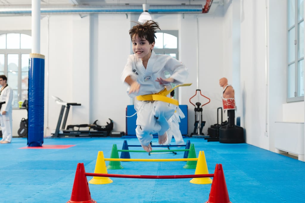 Bambino con cintura gialla salta un ostacolo colorato durante il percorso di agilità in palestra