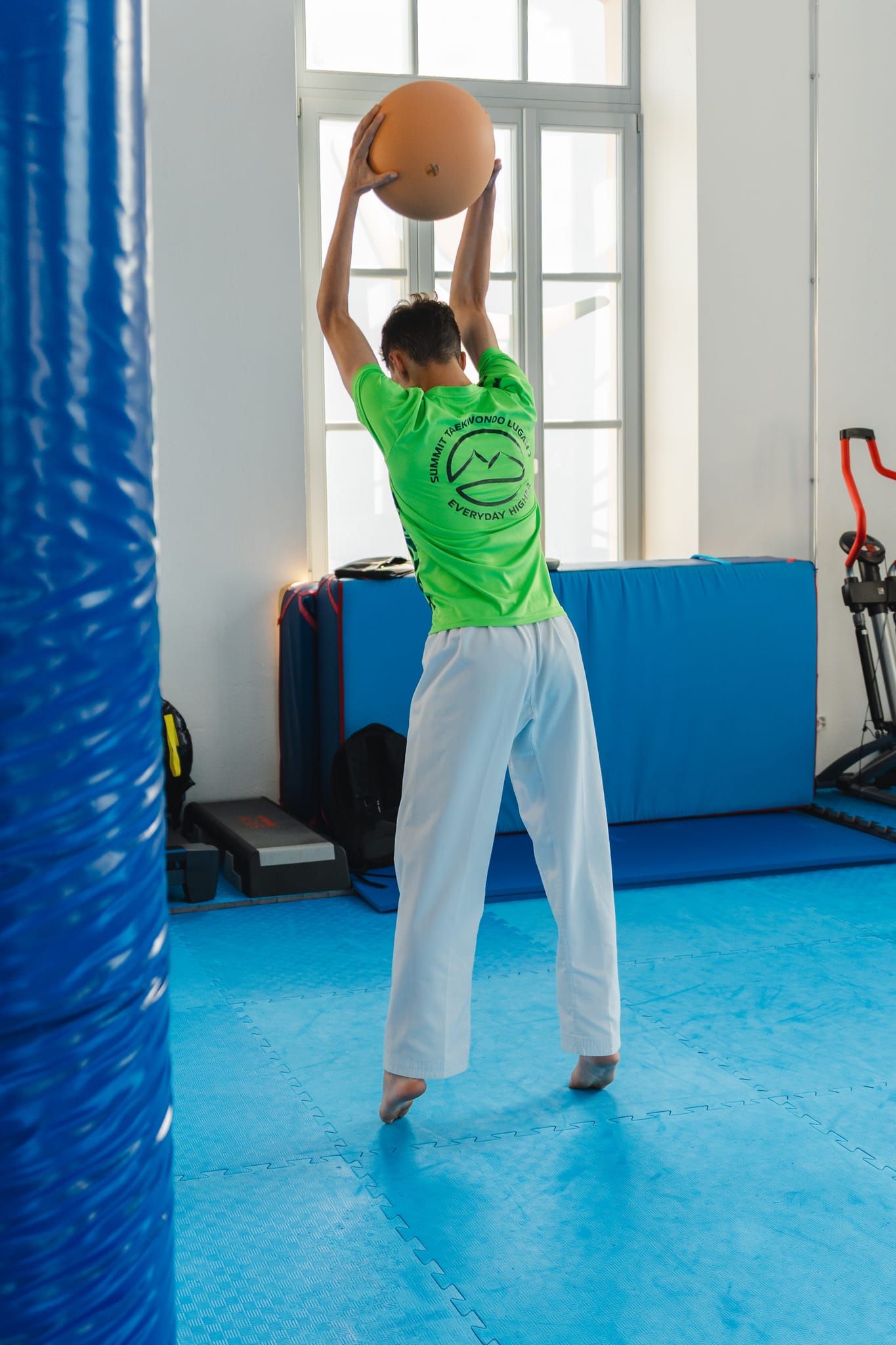 Ragazzo con maglietta Summit Taekwondo Lugano lancia una palla medica durante il condizionamento atletico in palestra
