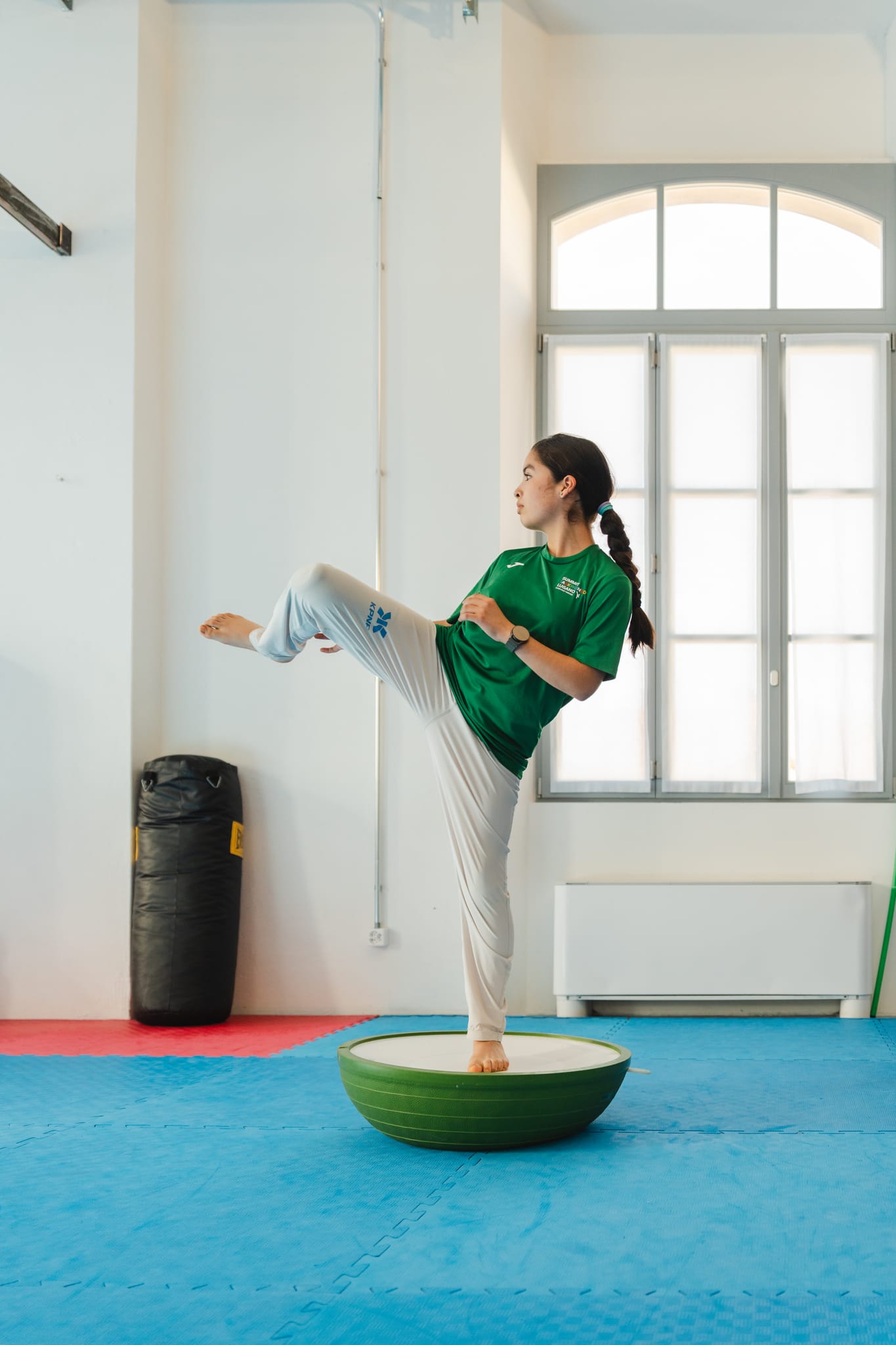 Giovane atleta in maglietta verde esegue un calcio laterale in equilibrio sulla cupola di allenamento